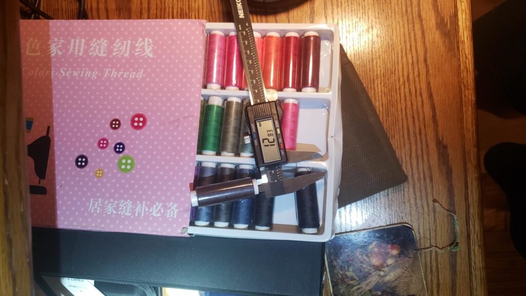 Box with assorted colors of thread on spools, digital calipers measuring the spool.